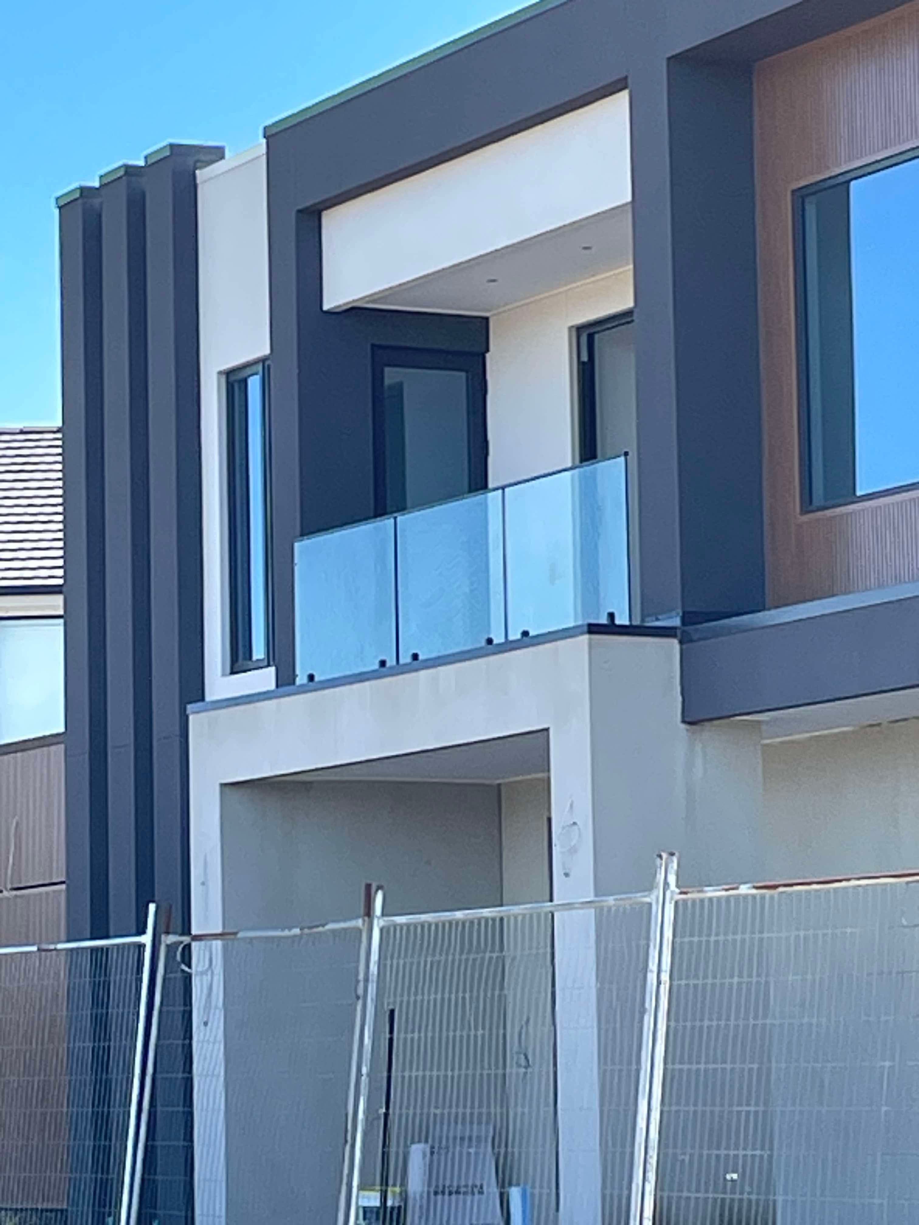 Clear glass balustrade with matte black spigots mounted along the edge of a first-floor balcony on a modern two-storey residential home under construction.