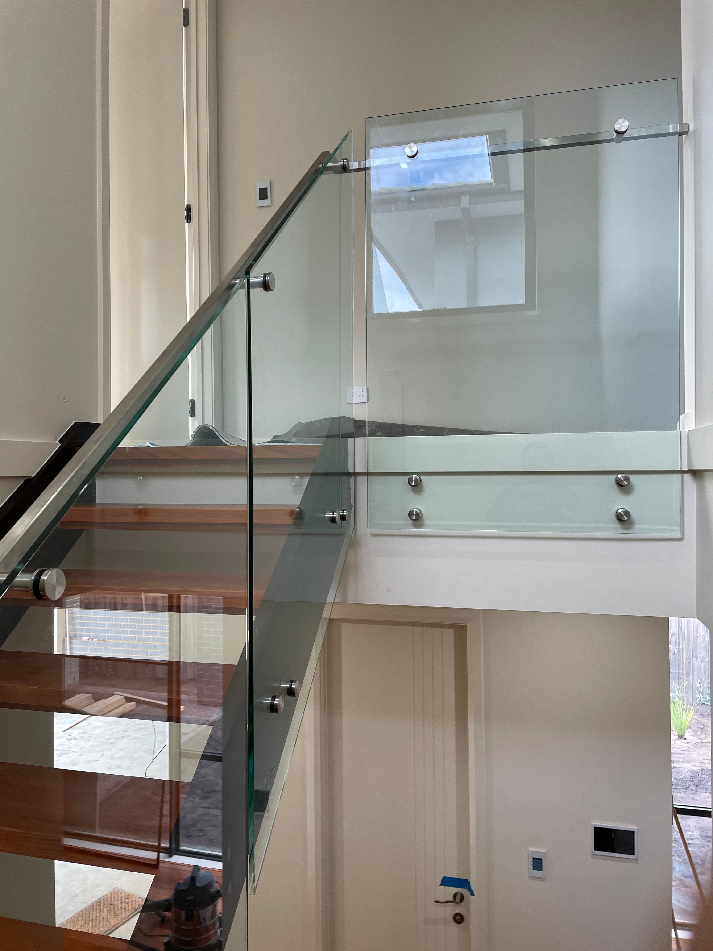 Clear glass staircase and landing balustrade with brushed nickel standoff fixings, installed on timber-treaded open stairs and mezzanine level in a contemporary home interior.