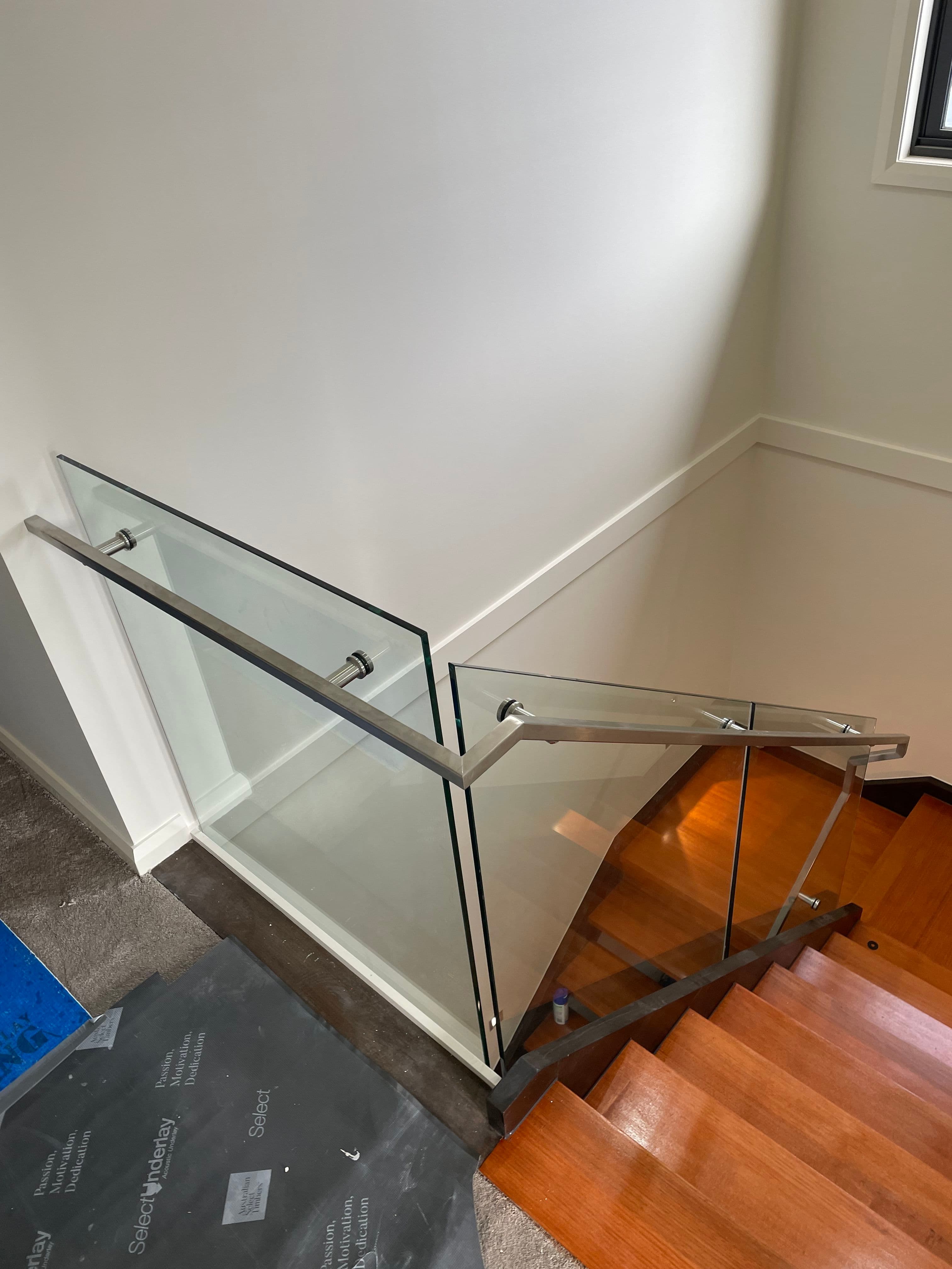 Clear glass stair and landing balustrade with brushed nickel standoff hardware and matching handrail channel on timber stairs in a contemporary interior.