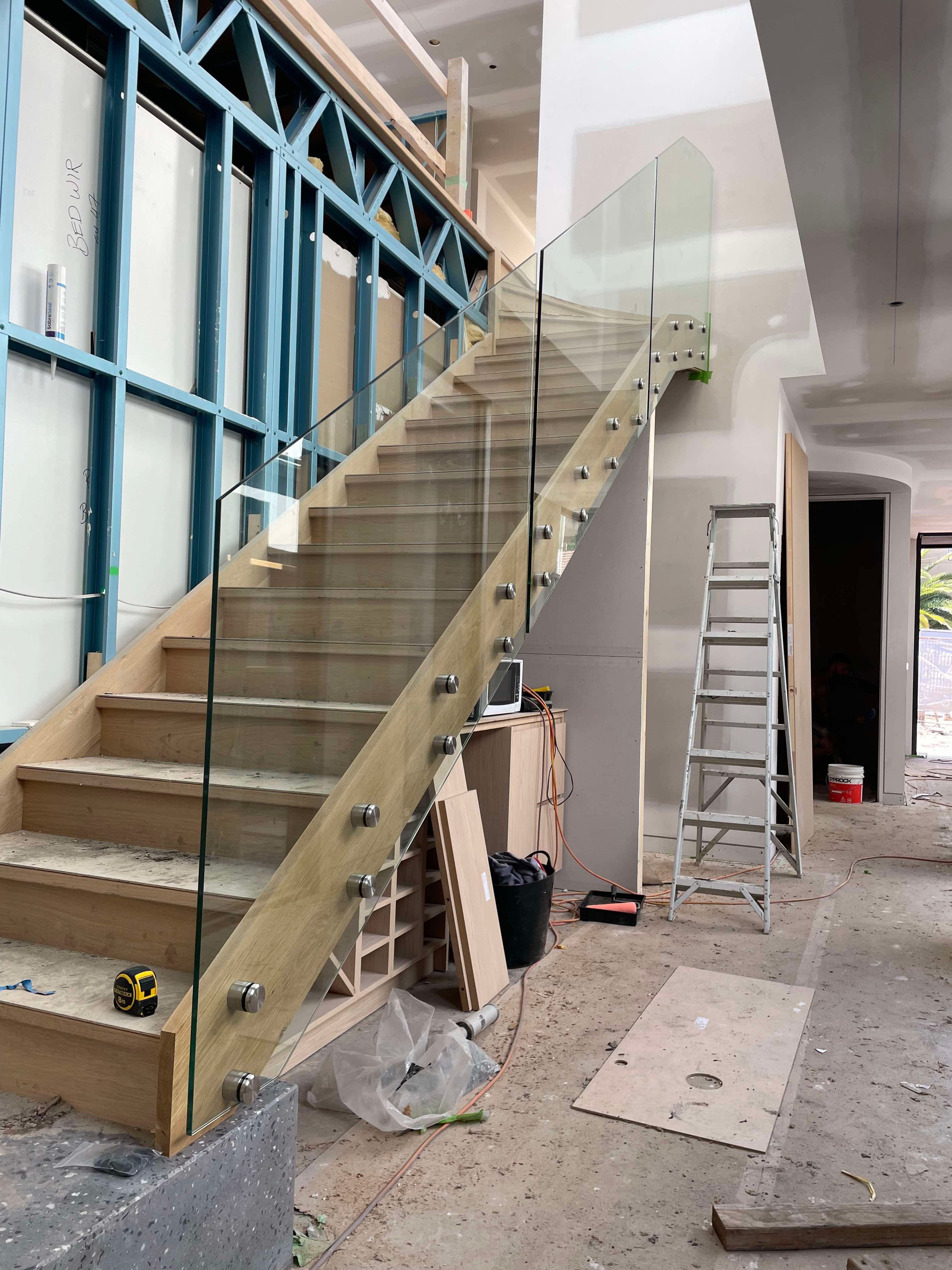 Clear glass staircase balustrade with brushed nickel standoff spigots mounted along timber stairs in a residential interior under construction.