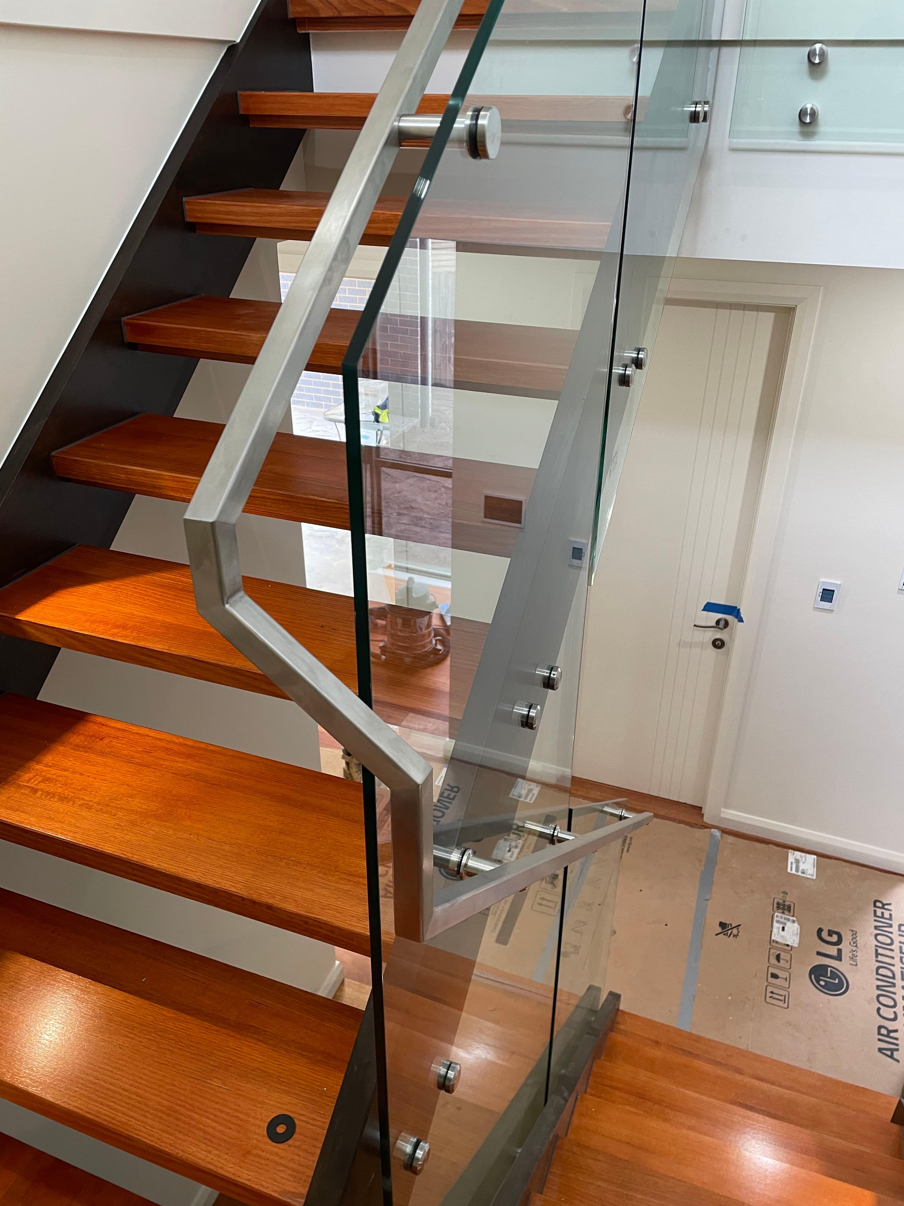 Clear glass staircase balustrade with brushed nickel standoff fixings and matching handrail brackets on open timber stairs inside a modern residential interior.
