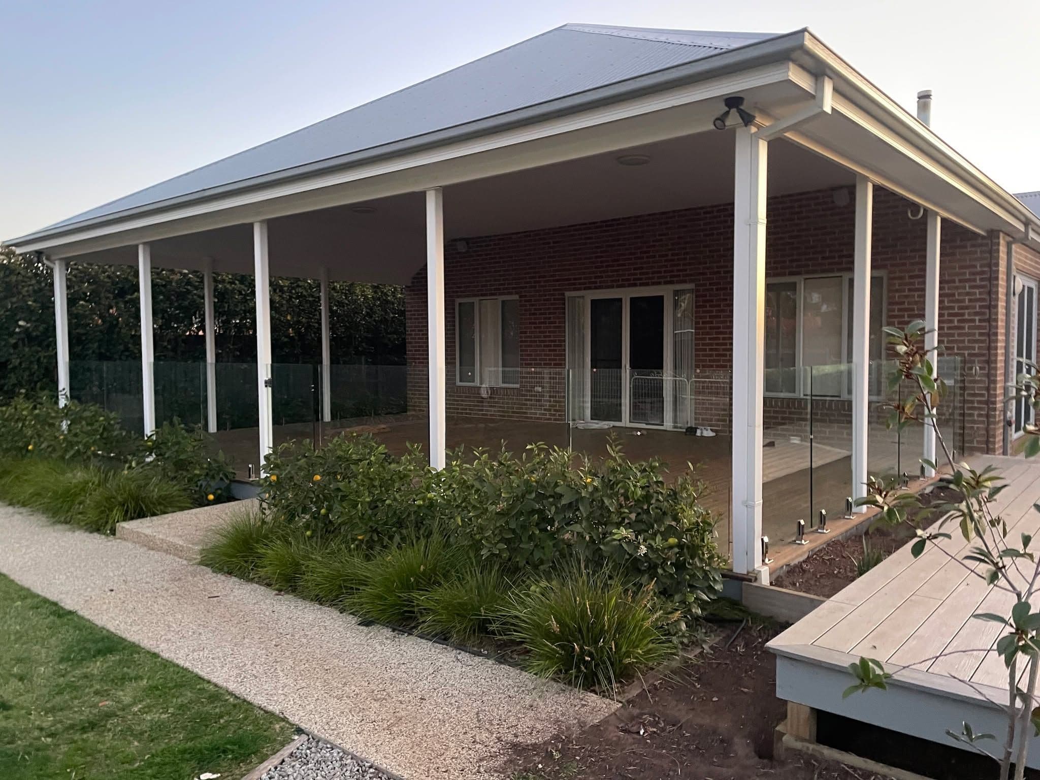 Frameless glass balustrade with spigots fixed into a timber deck surrounding an alfresco entertaining area on a brick residential home exterior.