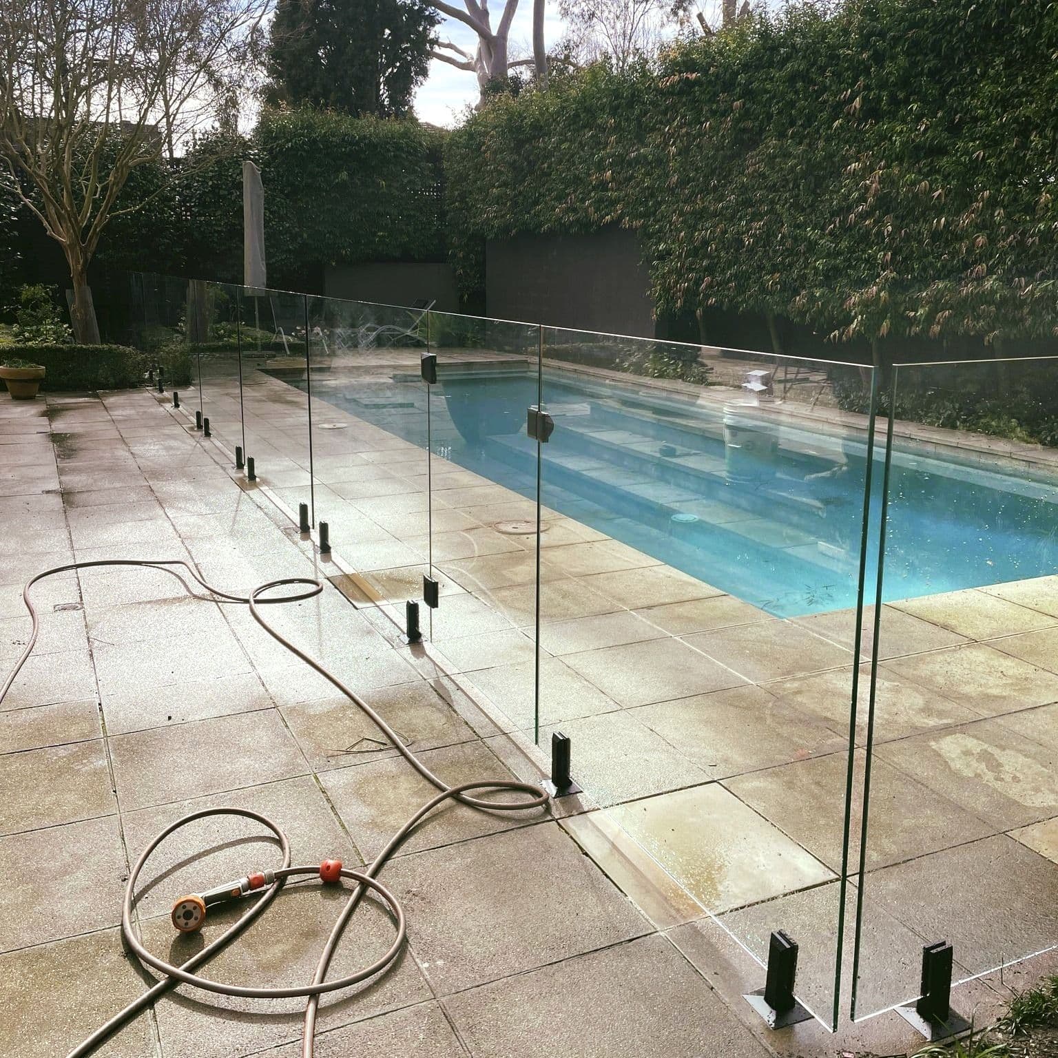 Frameless glass pool fence with matte black spigots core-drilled into stone coping surrounding a rectangular backyard swimming pool.