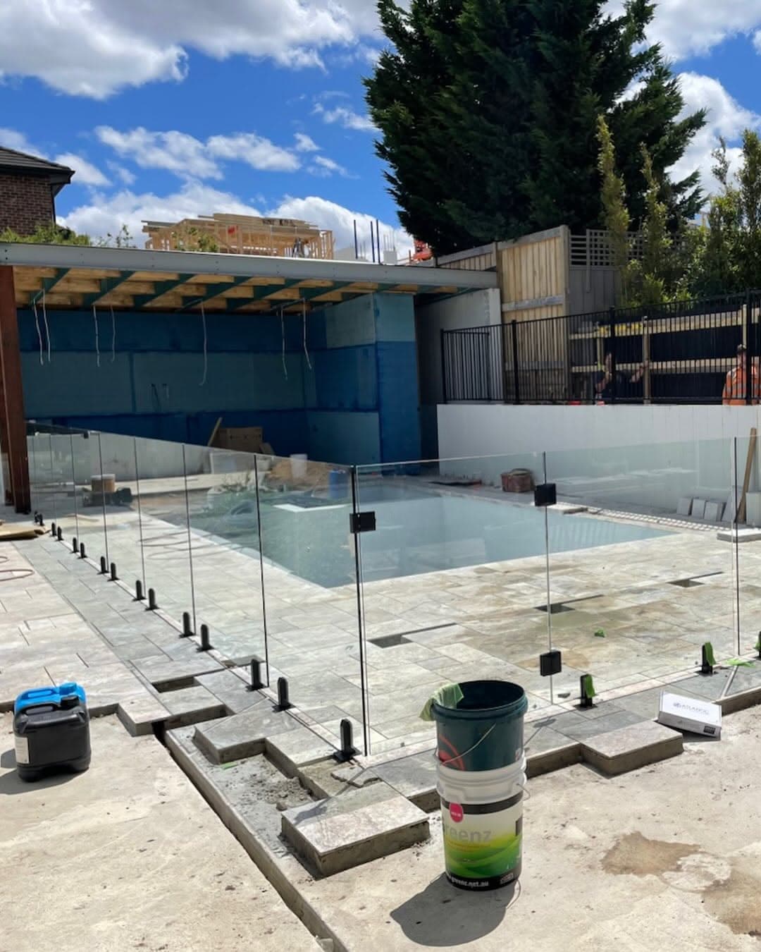 Frameless glass pool fence with matte black spigots core-drilled into stone coping surrounding a residential pool under construction.