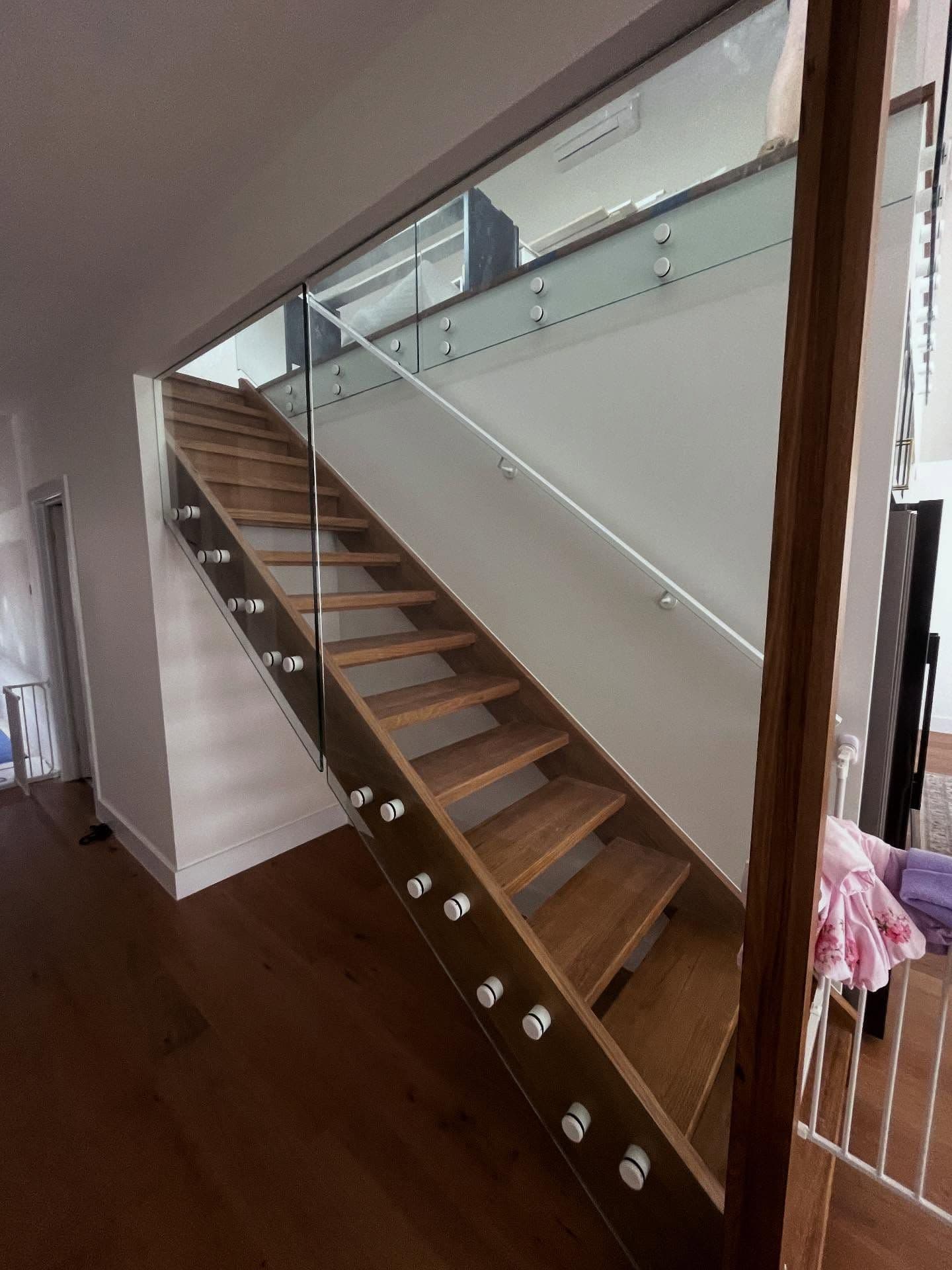 Glass stair balustrade with chrome standoff fixings running alongside timber staircase in a modern residential interior.
