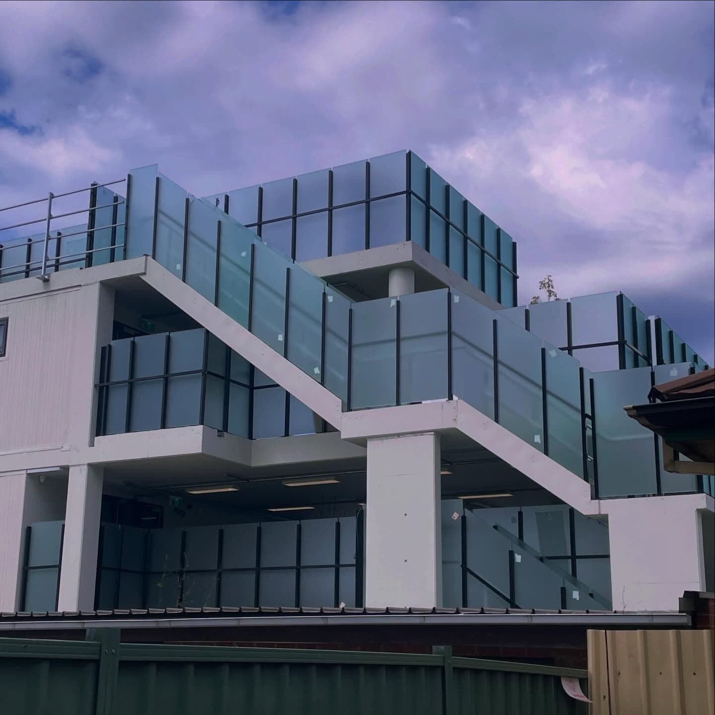 Large-scale glass balustrade installation across multiple levels of a modern commercial or residential building, featuring tinted glass panels with dark framing channels on elevated balconies and terraces.