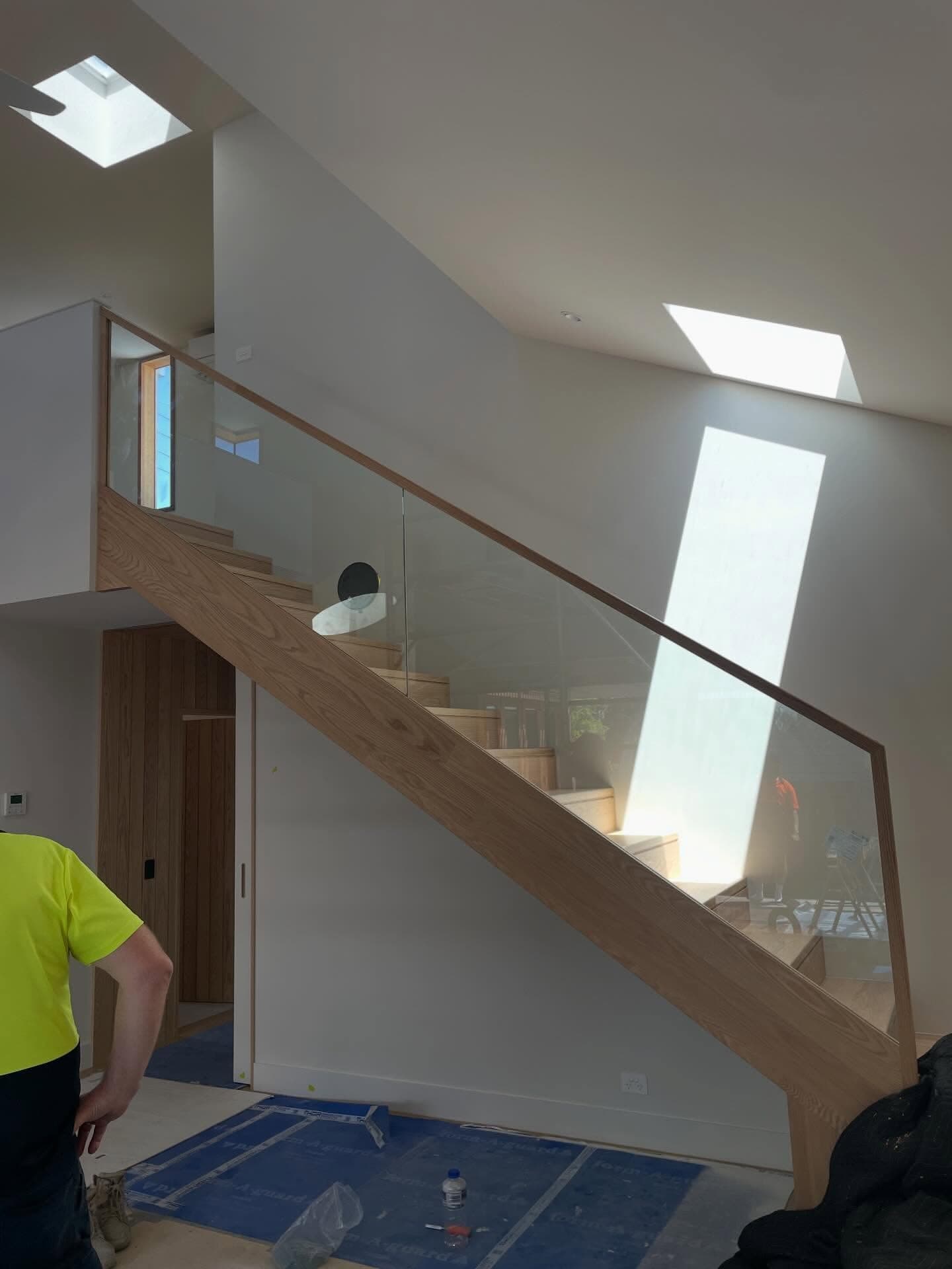 Clear glass staircase balustrade with timber handrail and timber string, installed on an internal staircase in a contemporary home with skylights.