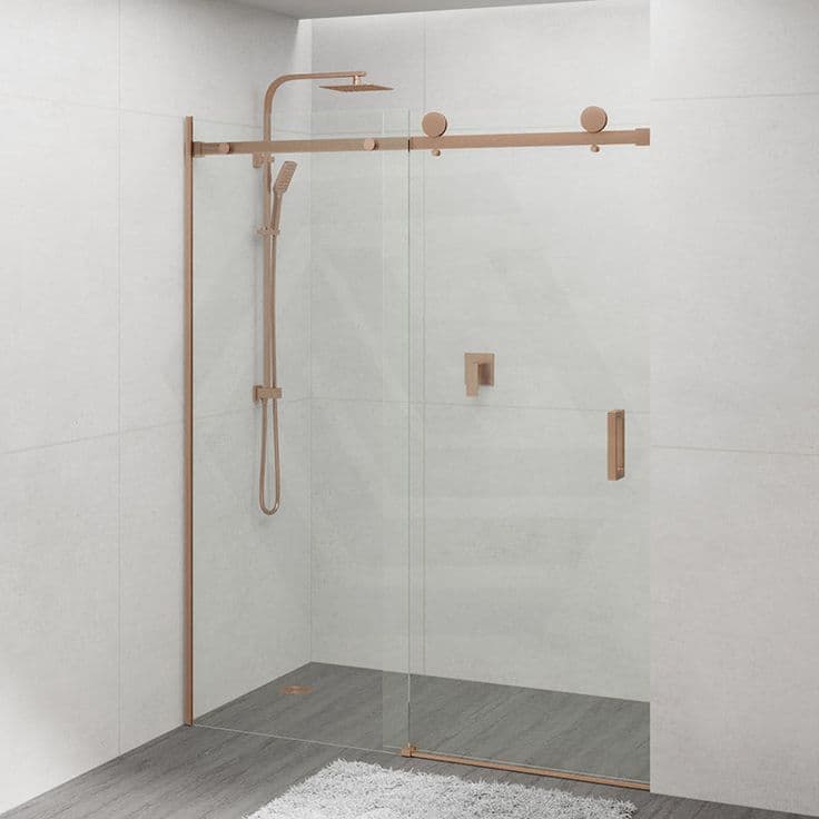 Semi-frameless sliding shower screen with a visible brushed gold (copper) top rail, sliding track hardware, and side channel in a minimal white tiled bathroom.