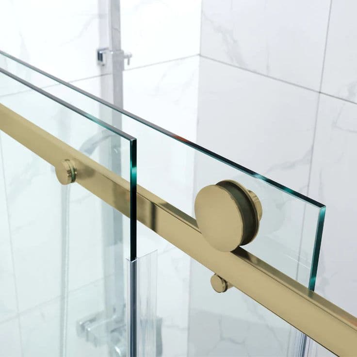 Semi-frameless shower screen with a brushed gold top rail and sliding door roller hardware in a white marble-tiled bathroom.