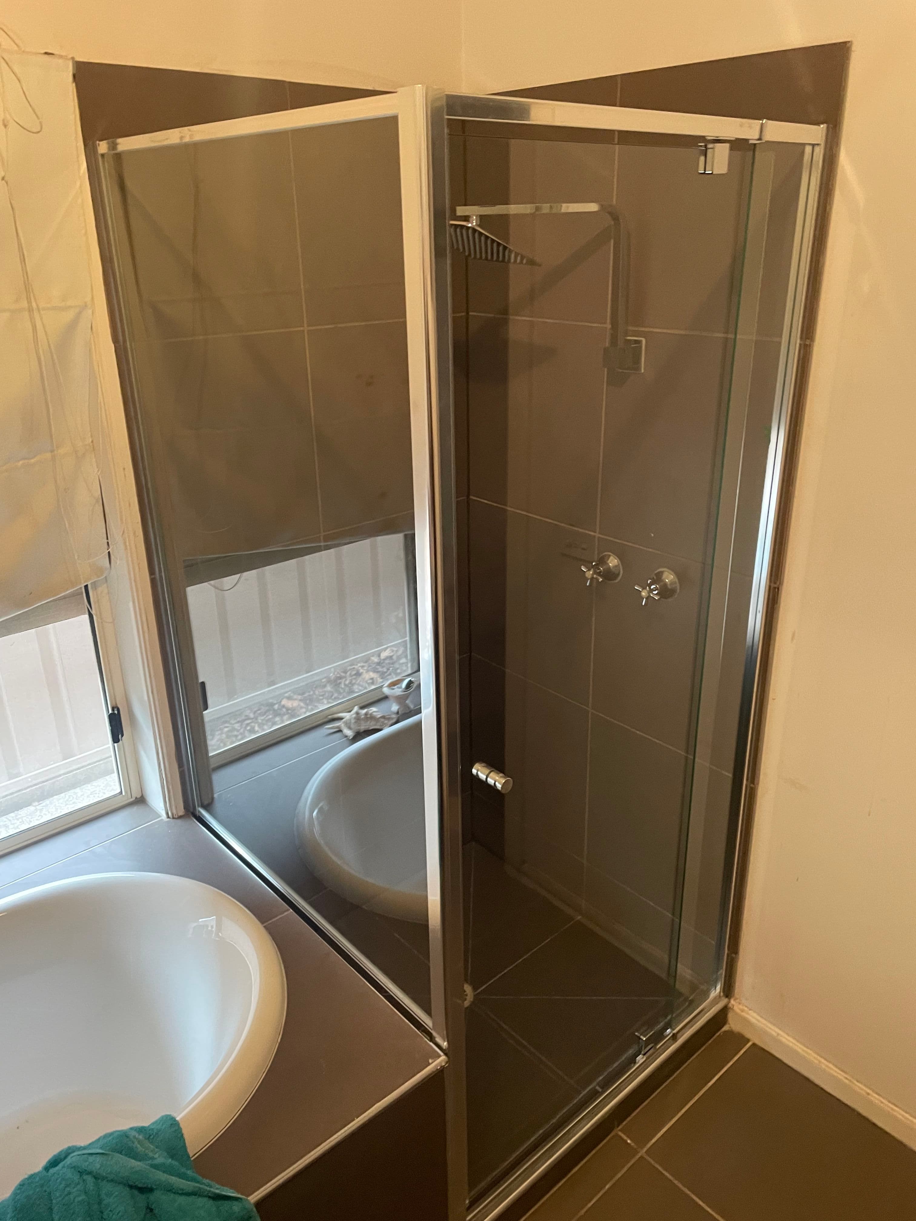 Semi-frameless shower enclosure with chrome aluminium framing on all edges, featuring a hinged door and fixed side panel in a dark grey tiled bathroom with a freestanding bath visible.