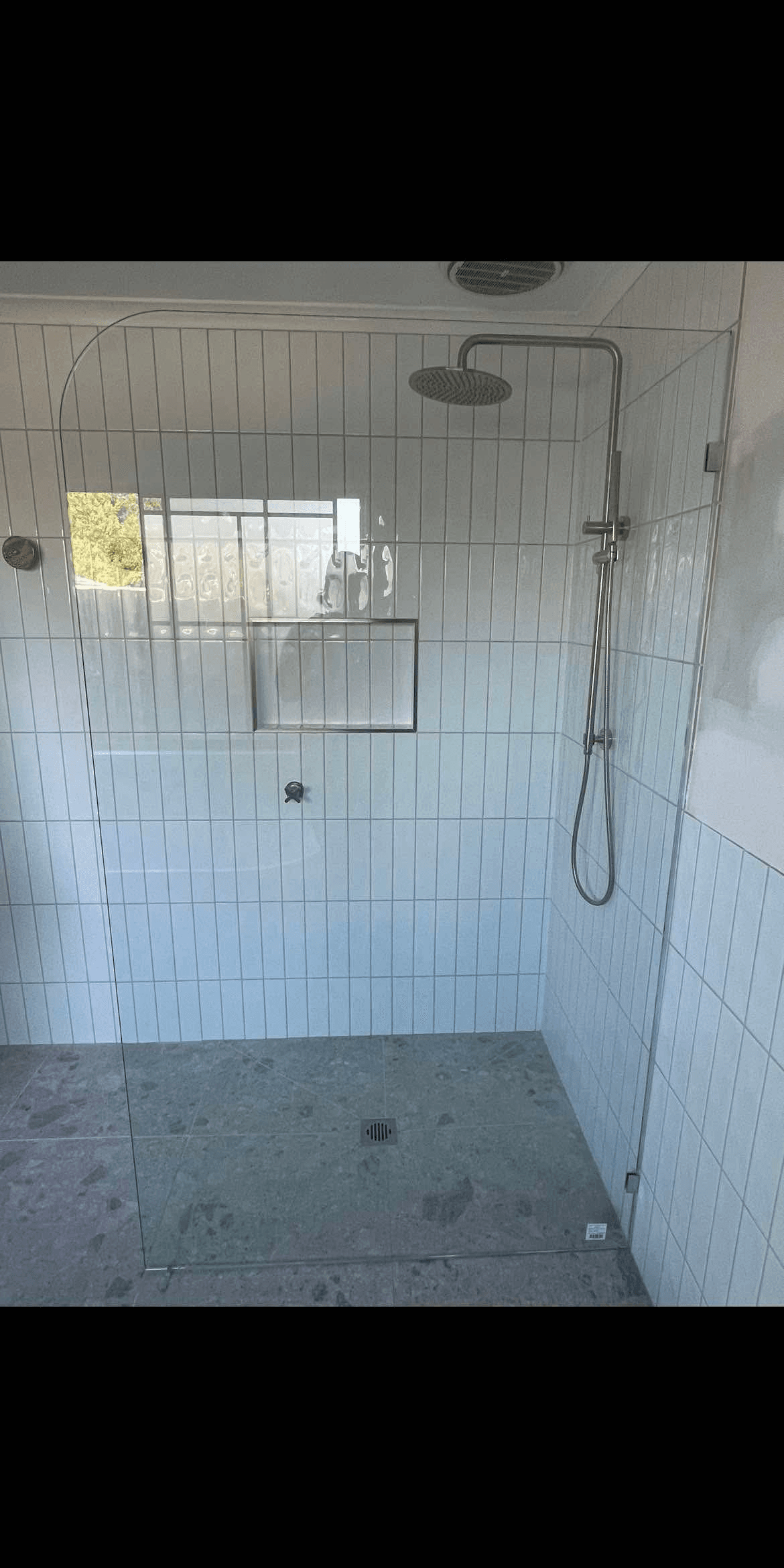 Frameless shower screen with a curved return panel and brushed nickel wall channel, clear glass in an open walk-in configuration with white vertical subway tiles and stone mosaic floor.