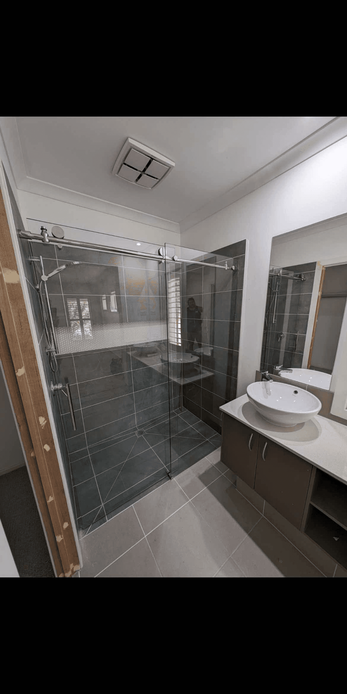 Semi-frameless sliding shower screen with a visible chrome top rail and sliding track in a dark-tiled bathroom with a vessel sink vanity.