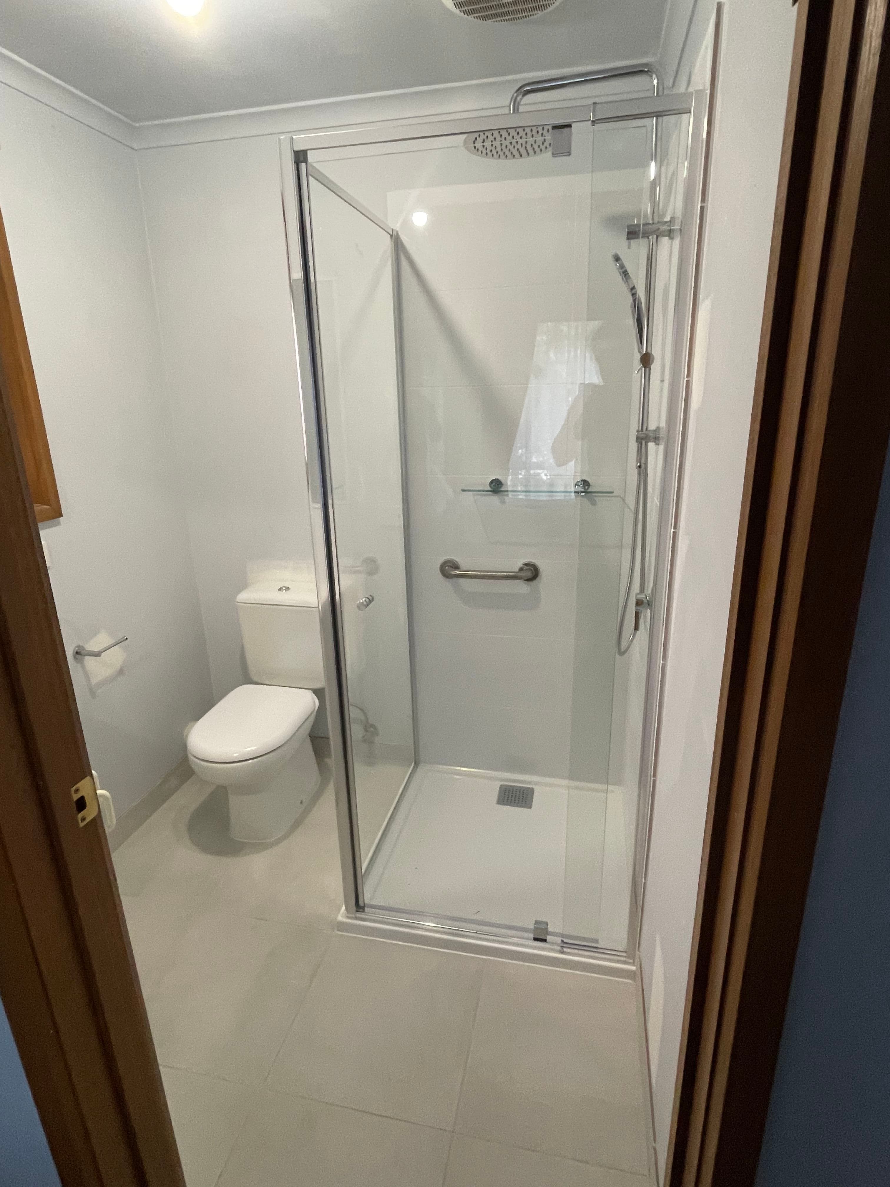 Semi-frameless shower enclosure with chrome aluminium frame rails and pivot door in a compact white bathroom with a shower base and toilet.