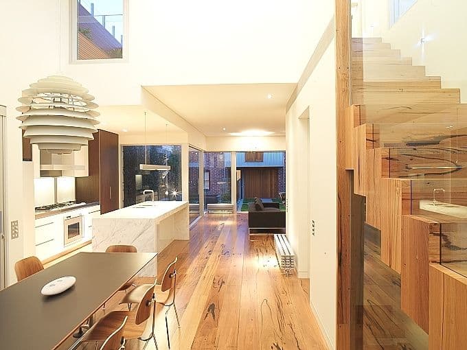 Frameless glass balustrade panels flanking a timber staircase in a contemporary open-plan home interior with hardwood flooring.