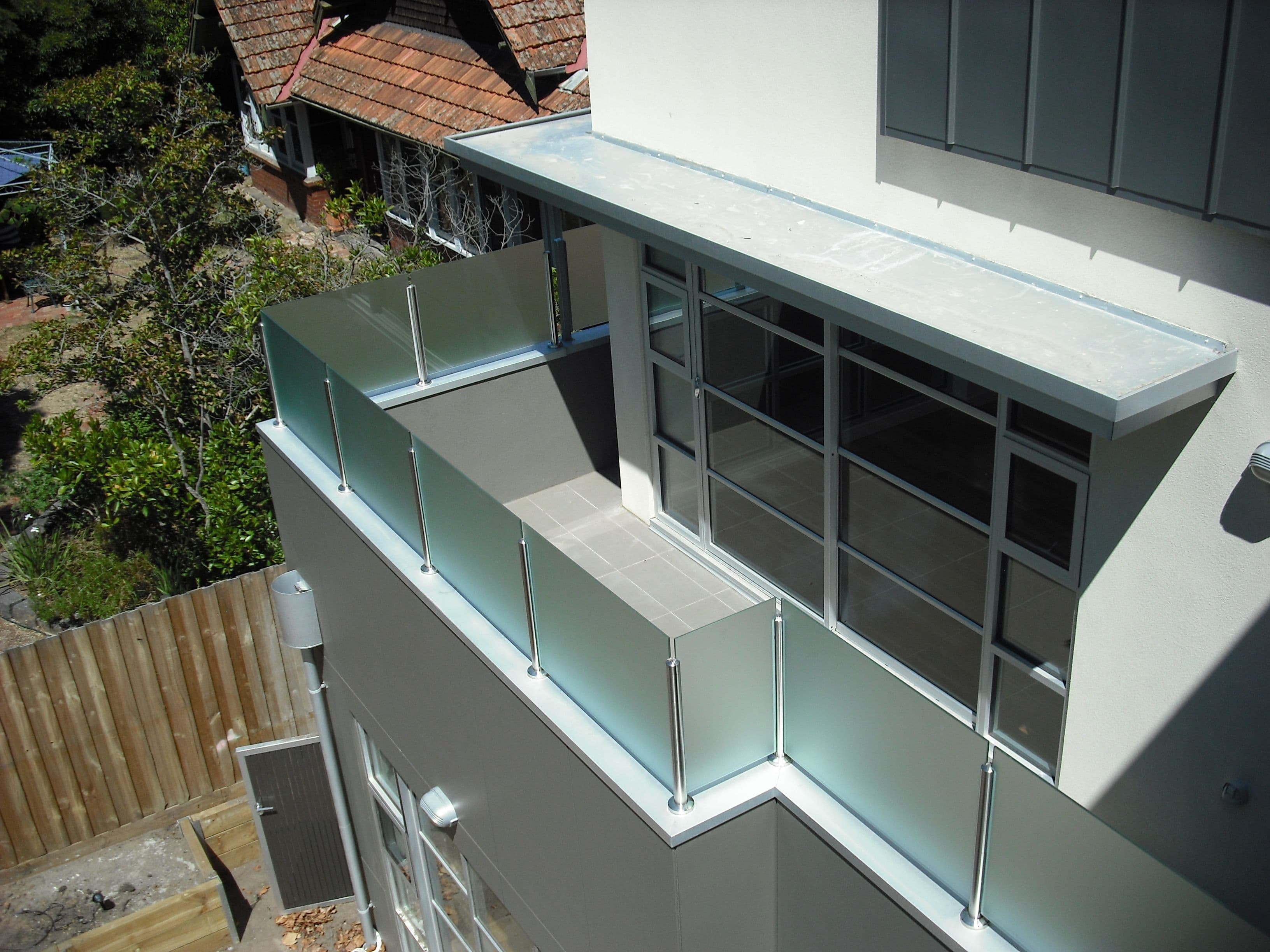 Acid etched glass balustrade panels with chrome spigots fixed to the edge of an elevated tiled balcony on a modern multi-storey residential building, with no pool visible.