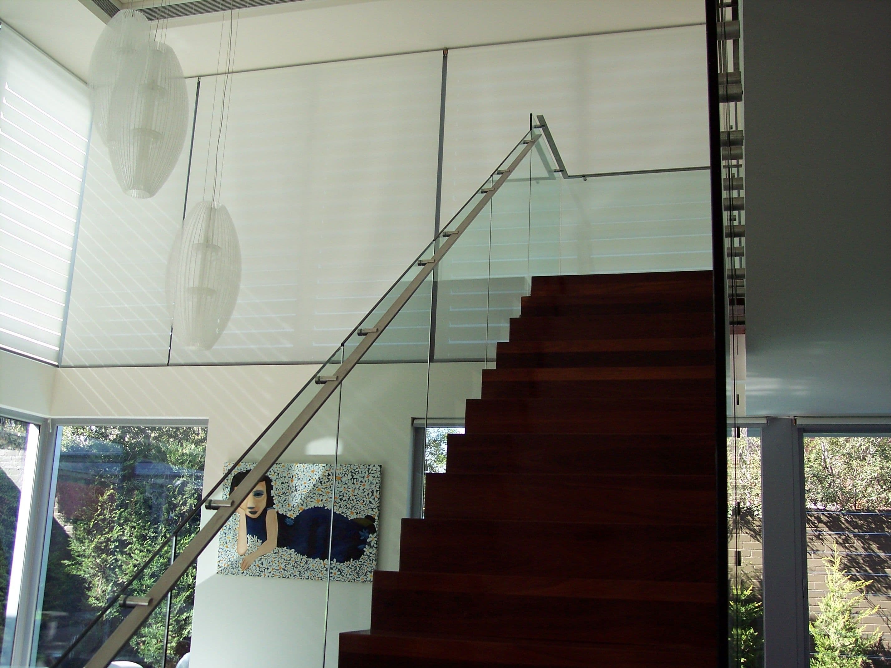 Frameless glass staircase balustrade with brushed nickel standoff hardware running alongside dark timber stairs in a contemporary open-plan interior.