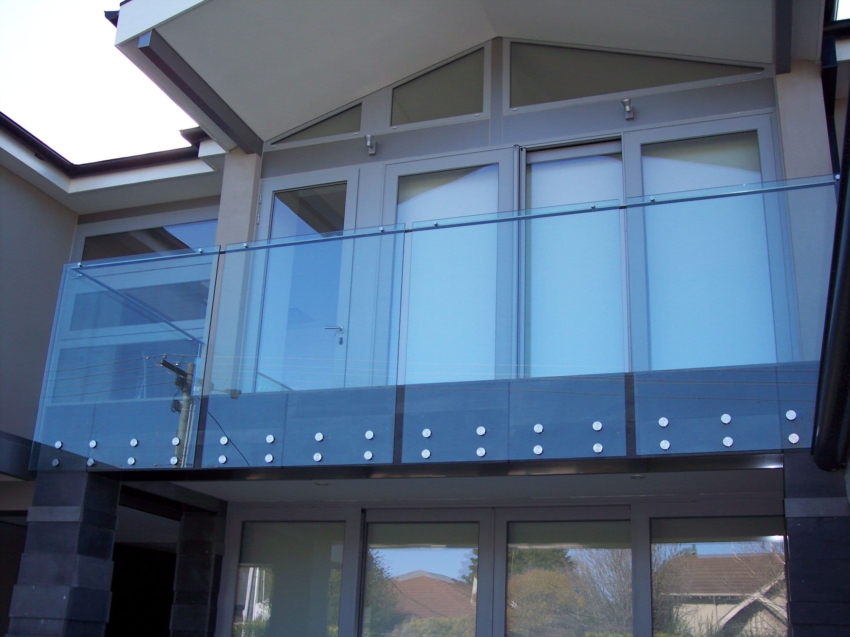 Clear glass balustrade with chrome point-fix button fixings and a top aluminium handrail channel on a first-floor balcony of a modern residential home.