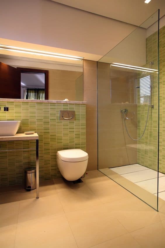 Frameless shower screen configured as a single fixed panel with no visible aluminium framing or hinges, creating an open walk-in shower in a modern tiled bathroom with green mosaic feature tiles.