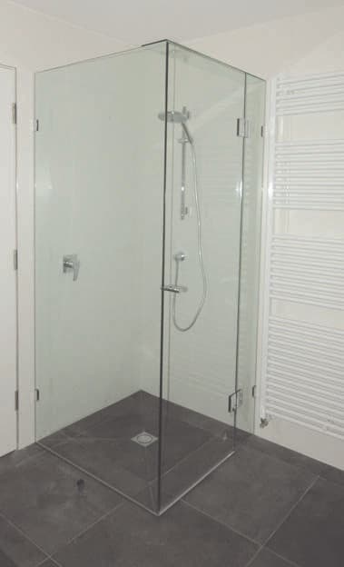 Frameless shower enclosure in a corner configuration with chrome hinges mounted directly onto clear glass panels, set in a white bathroom with dark grey slate-style floor tiles.