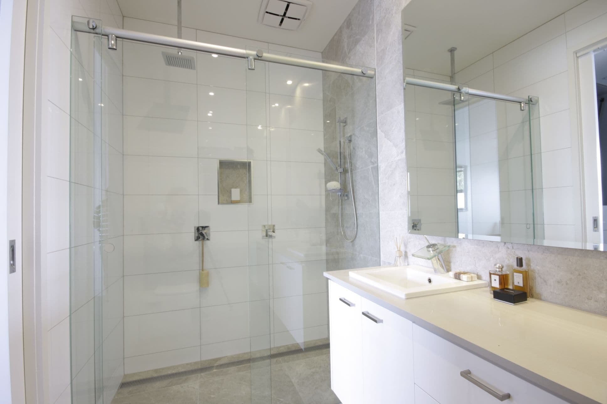 Semi-frameless sliding shower screen with a visible aluminium top rail and chrome hardware in a modern tiled bathroom with a floating vanity.