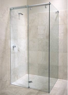 Semi-frameless shower enclosure with a sliding door on a visible top aluminium rail and chrome hardware, forming an L-shaped configuration in a marble-tiled bathroom.
