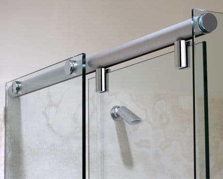 Semi-frameless sliding shower screen with a visible chrome aluminium top rail and chrome wall-mounted brackets, with clear glass panels in a marble-tiled bathroom.