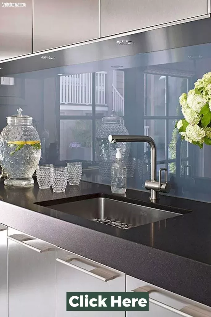 Smoke grey glass splashback mounted behind a kitchen sink with brushed nickel tapware, dark stone benchtop, and white cabinetry in a modern kitchen.