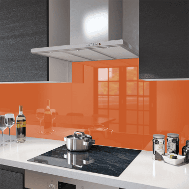 Vibrant orange toughened glass splashback mounted flush behind a black induction cooktop in a modern dark and white kitchen with stainless steel rangehood.