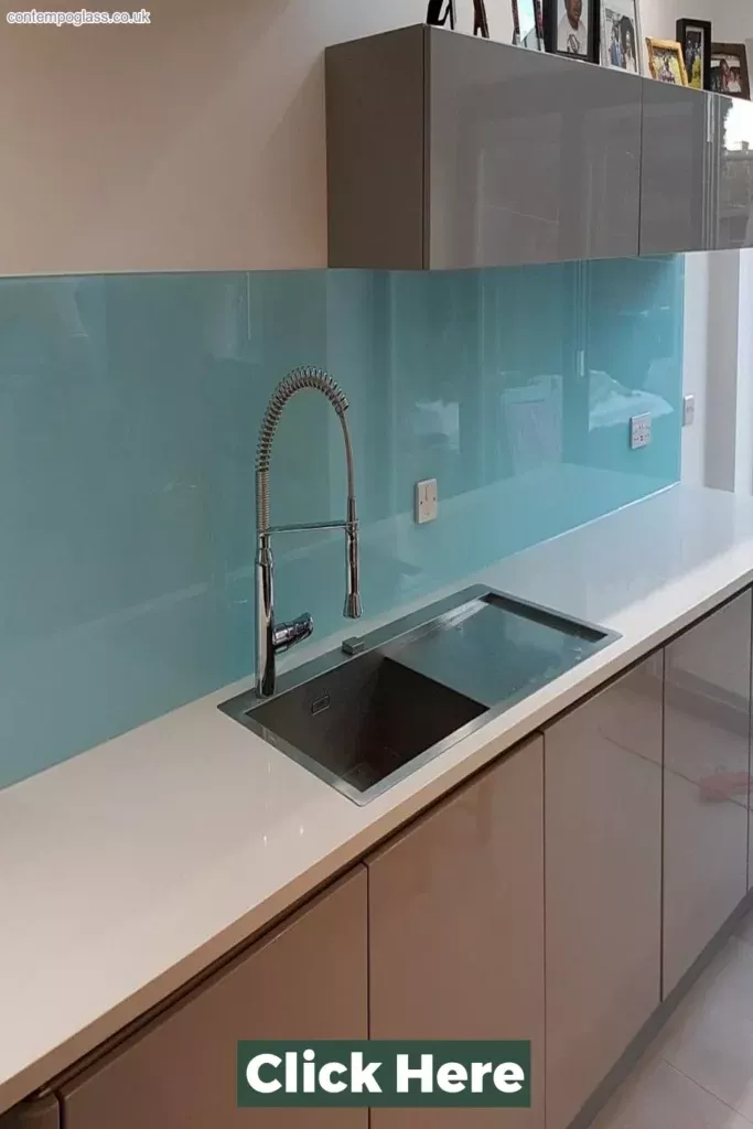 Light blue tinted glass splashback mounted flush on the wall behind a stainless steel sink with a chrome spring-neck tap in a modern kitchen with white benchtop and gloss cabinetry.
