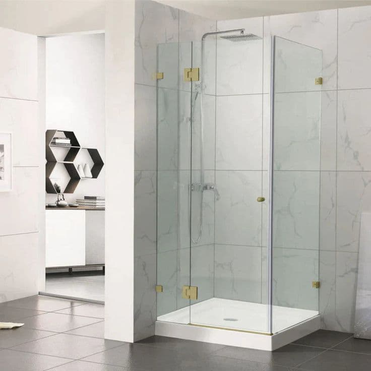 Frameless shower enclosure in a corner configuration with brushed gold hinges and clips mounted directly onto clear glass panels, set in a marble-tiled bathroom with a white shower base.