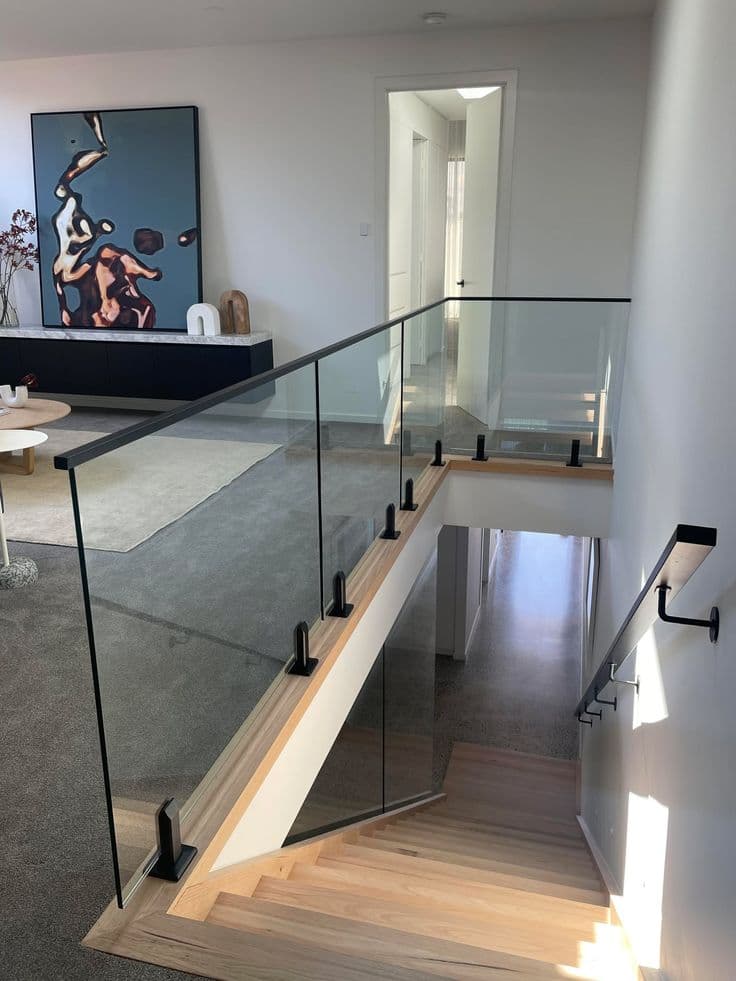 Clear glass staircase and mezzanine balustrade with matte black spigots and top handrail on timber-edged stairs in a modern interior home setting.