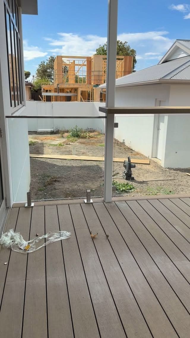 Clear glass balustrade panels with square spigots fixed to a composite deck on an alfresco area, with a construction site visible beyond.