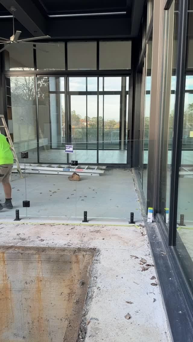 Frameless glass pool fence panels being installed with matte black square spigots core-drilled into concrete coping around what appears to be a newly constructed pool area at a modern residential property in Glen Iris.