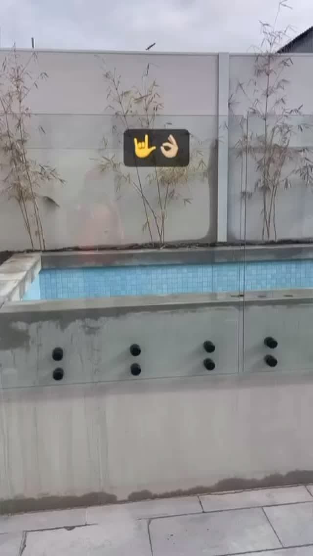 Frameless pool fence with matte black spigots core-drilled into concrete pool coping surrounding a tiled lap pool in an outdoor residential setting.