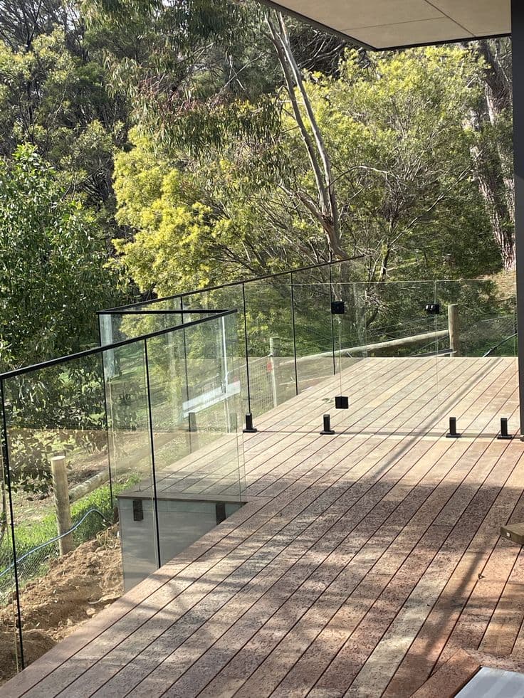 Frameless glass balustrade with matte black square spigots installed on a timber deck overlooking a bushland setting, no pool visible.